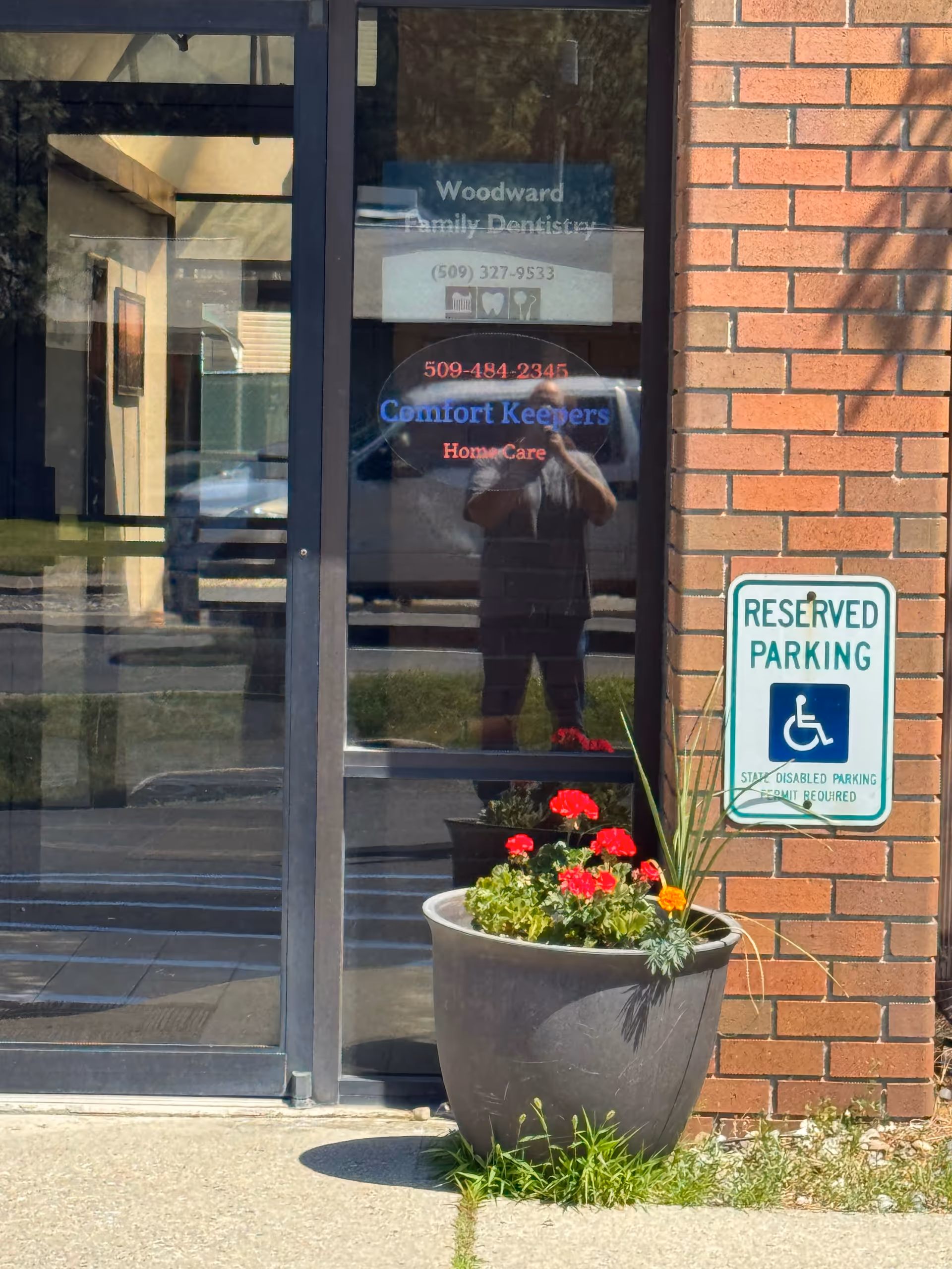 Front entrance of Comfort Keepers with a potted plant, brick wall, and reserved parking sign.