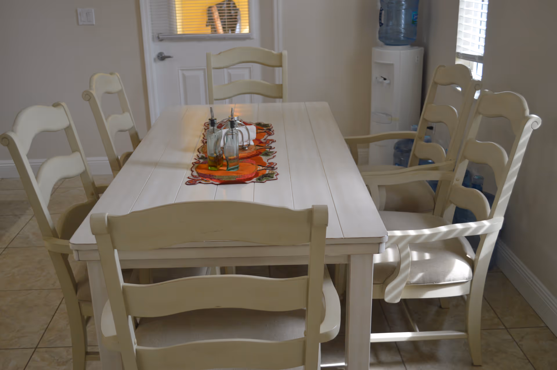 Cream-colored dining table with chairs in a bright communal dining room.