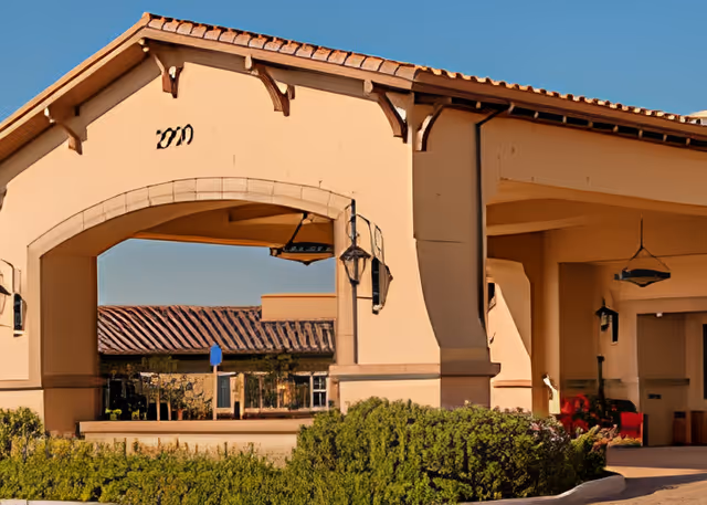 Front entrance porte-cochère of an assisted living building with an arched canopy, hanging lanterns, and landscaped shrubs.