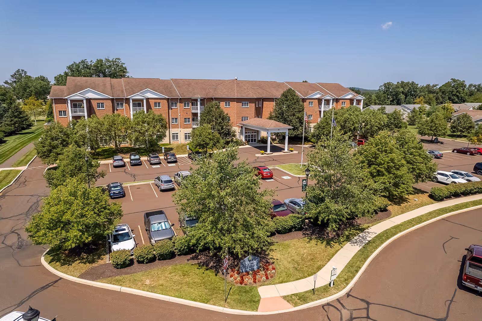 Exterior view of a brick senior living facility with parking and landscaped grounds.