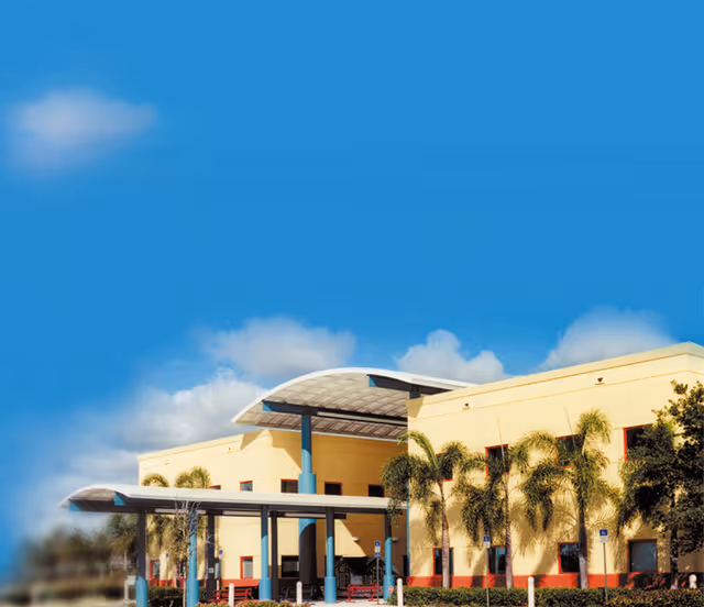 Sunny view of the outpatient center's yellow exterior with palm trees and teal entrance canopy.
