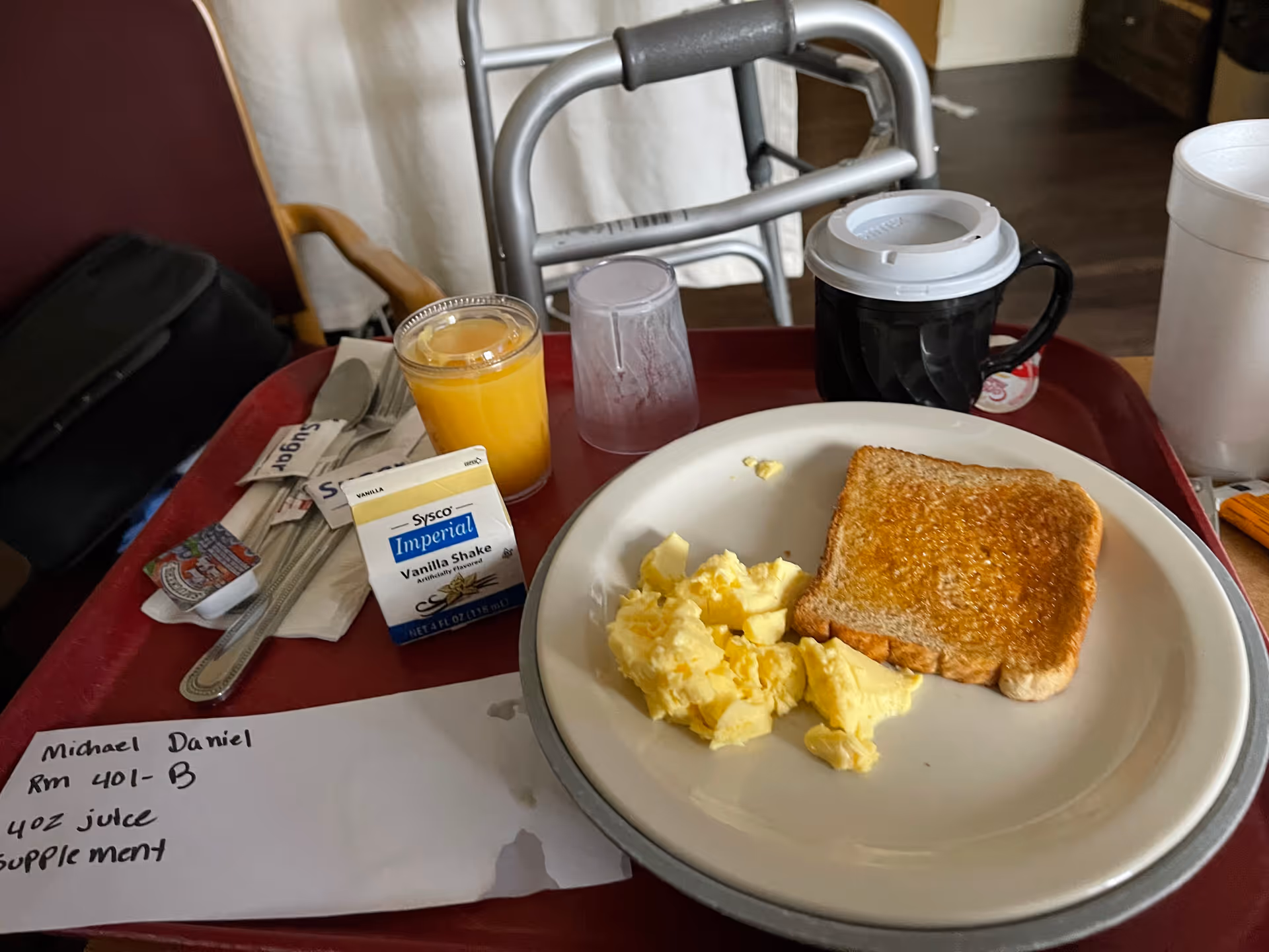 Meal on a red tray with toast, scrambled eggs, orange juice, and a nearby walker.