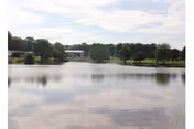 Tranquil lake with trees and a distant building on Quality Life Services Sugar Creek campus.