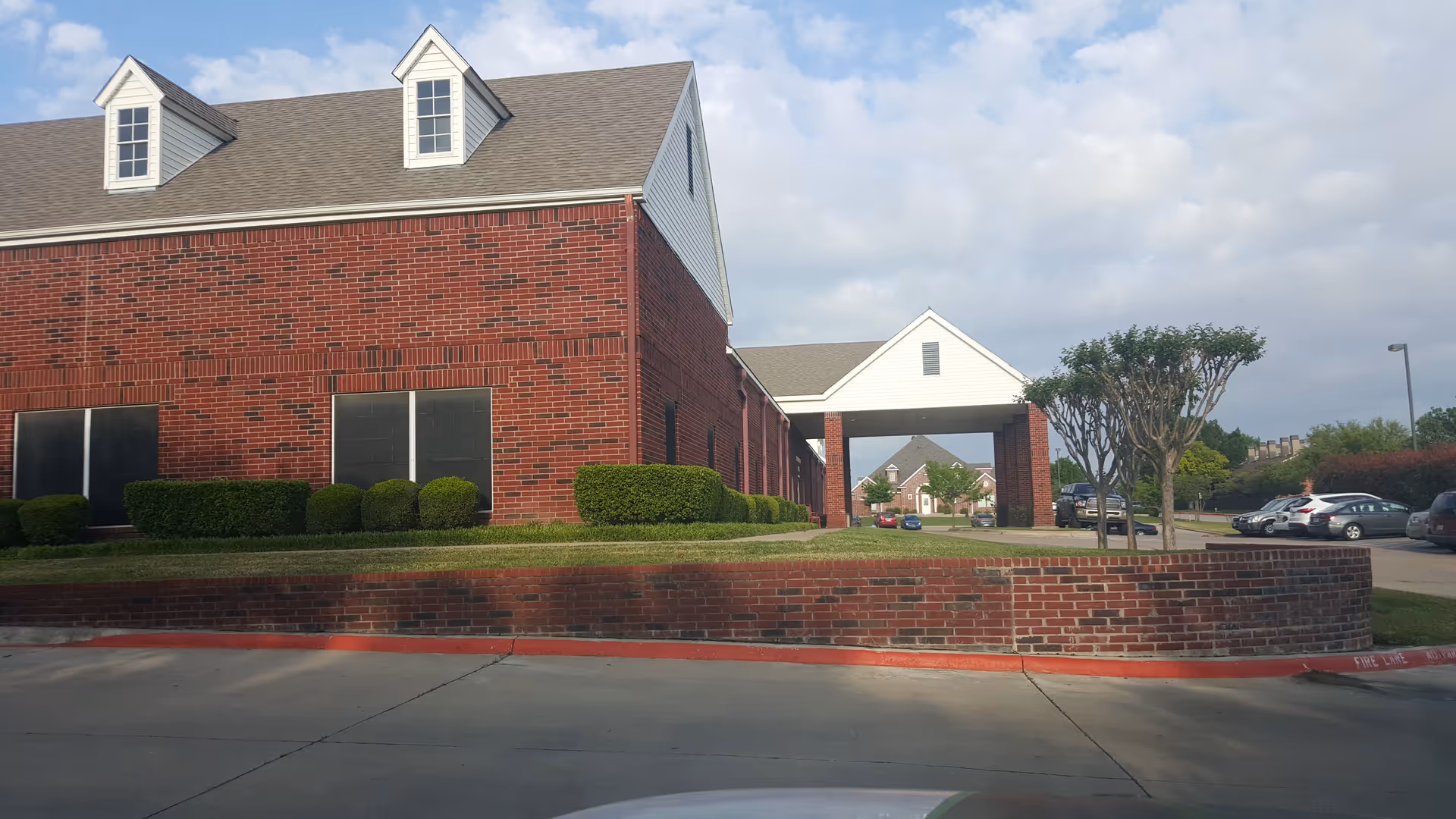 Red brick senior living facility with a covered entrance and hedges.