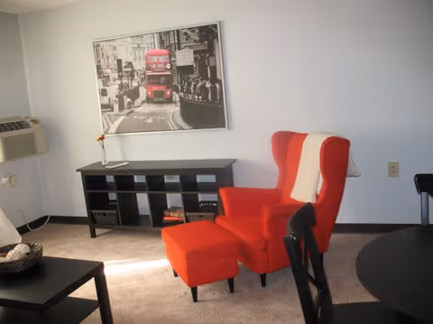 Red armchair with ottoman beside a black console table in a bright living area.