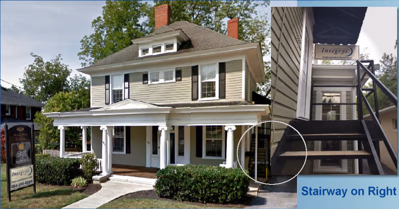 Front view of a two-story house-like building with a covered porch and right exterior stairs.