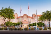 Front view of a pink senior living facility with flags, trees, and parked cars.