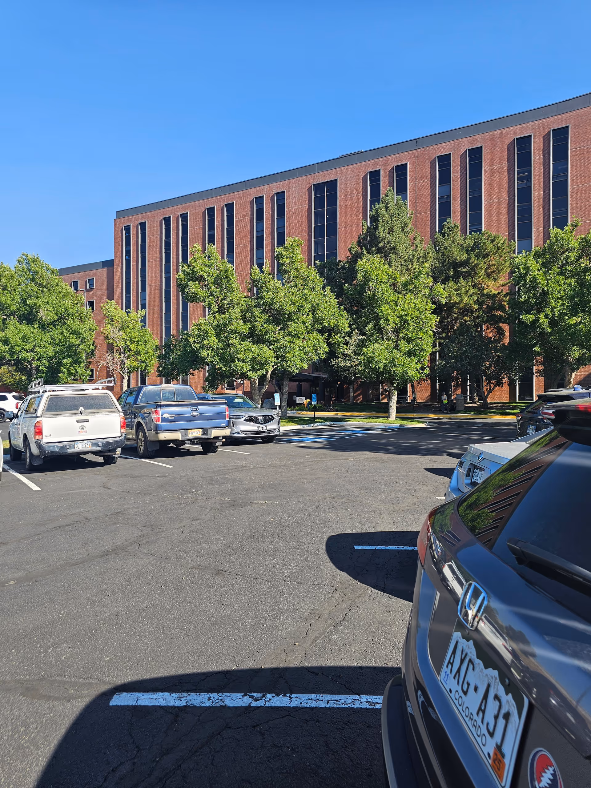 Exterior of a brick Pasco senior living building with parked cars and trees.