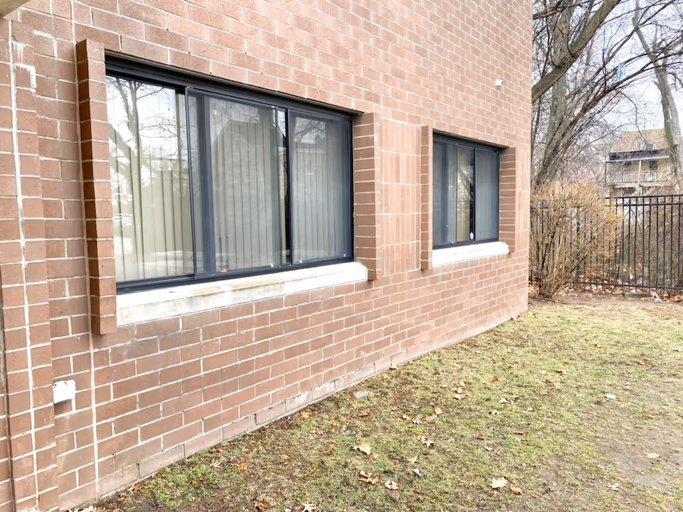 Brick exterior of a building with two large windows and a grassy yard
