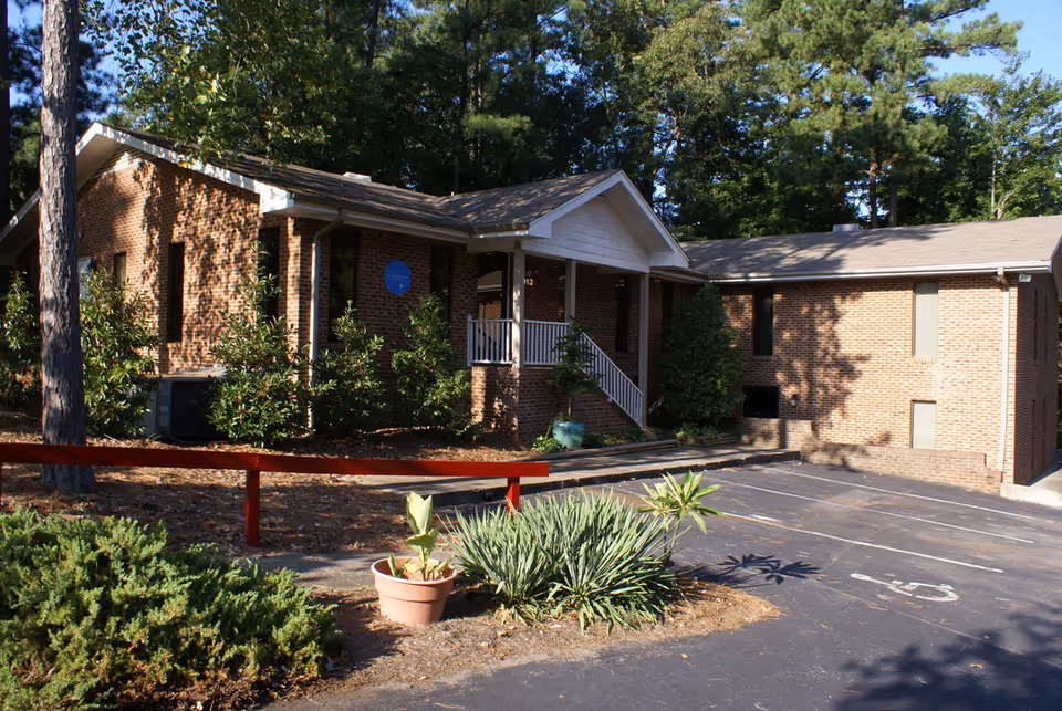 Brick senior living facility exterior with entrance porch, steps, parking, and trees.