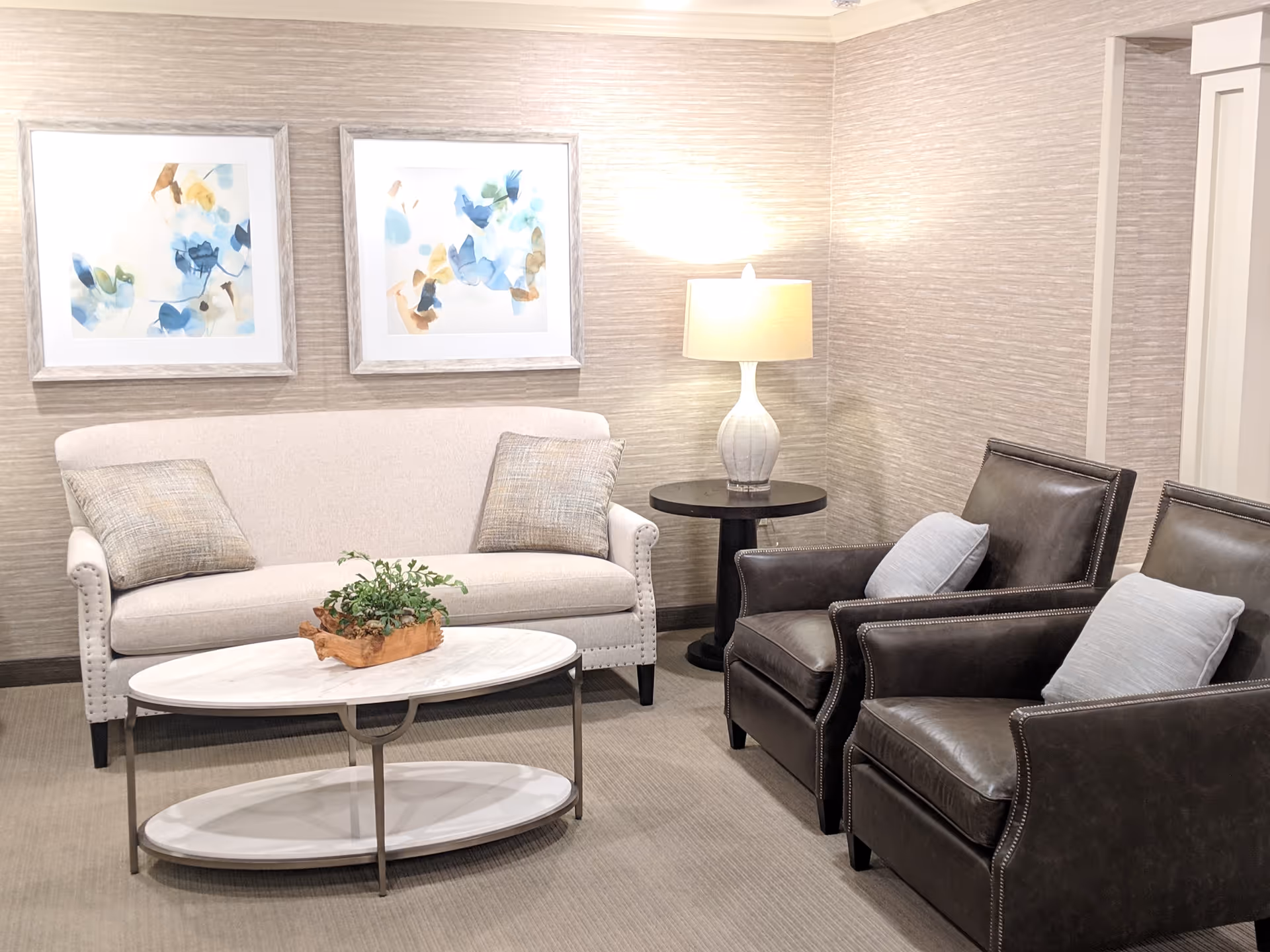 Cozy lounge area with a white sofa, two dark leather chairs, coffee table, and wall art.