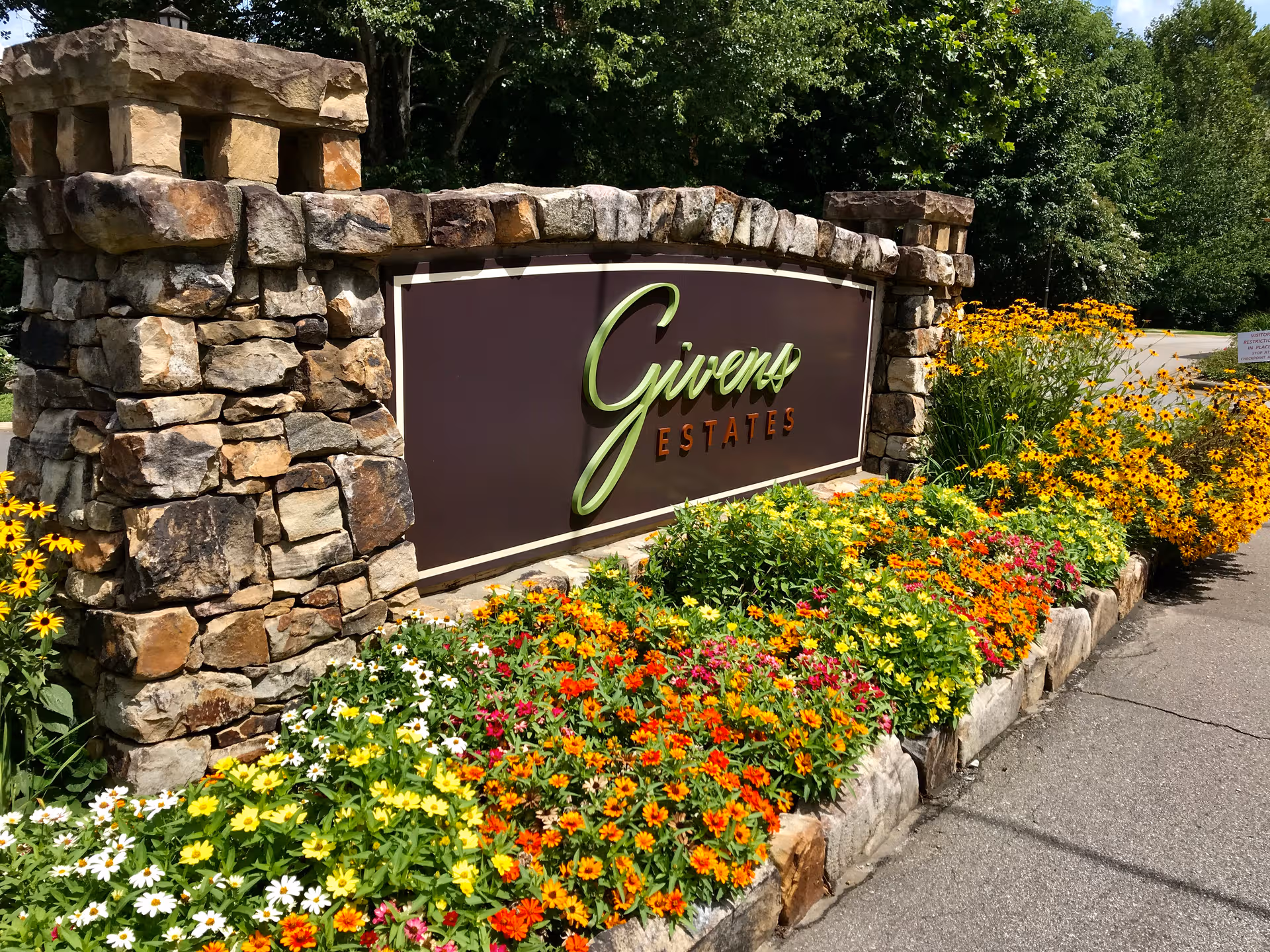 Stone entrance sign reads Givens Estates, surrounded by colorful flower beds and greenery.