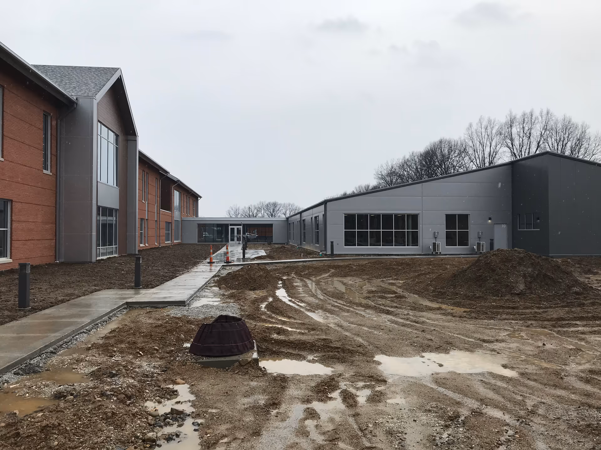 Construction site in front of a modern senior living facility, with muddy ground and new buildings.