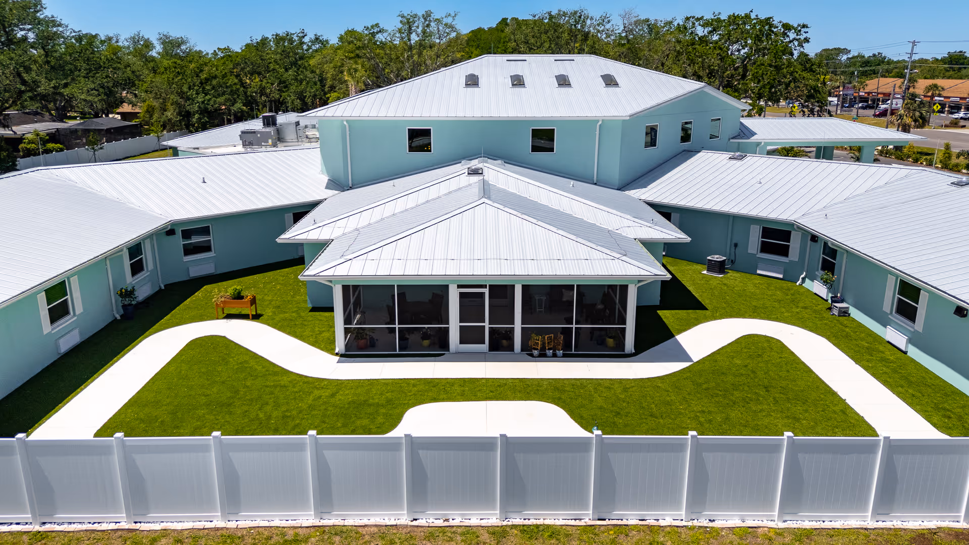 Aerial view of a light-blue senior living facility with manicured lawn and curved pathways.