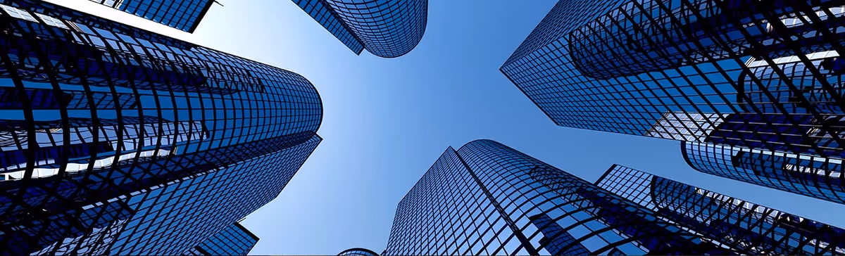 Tall blue glass skyscrapers converge toward a clear sky from ground level.