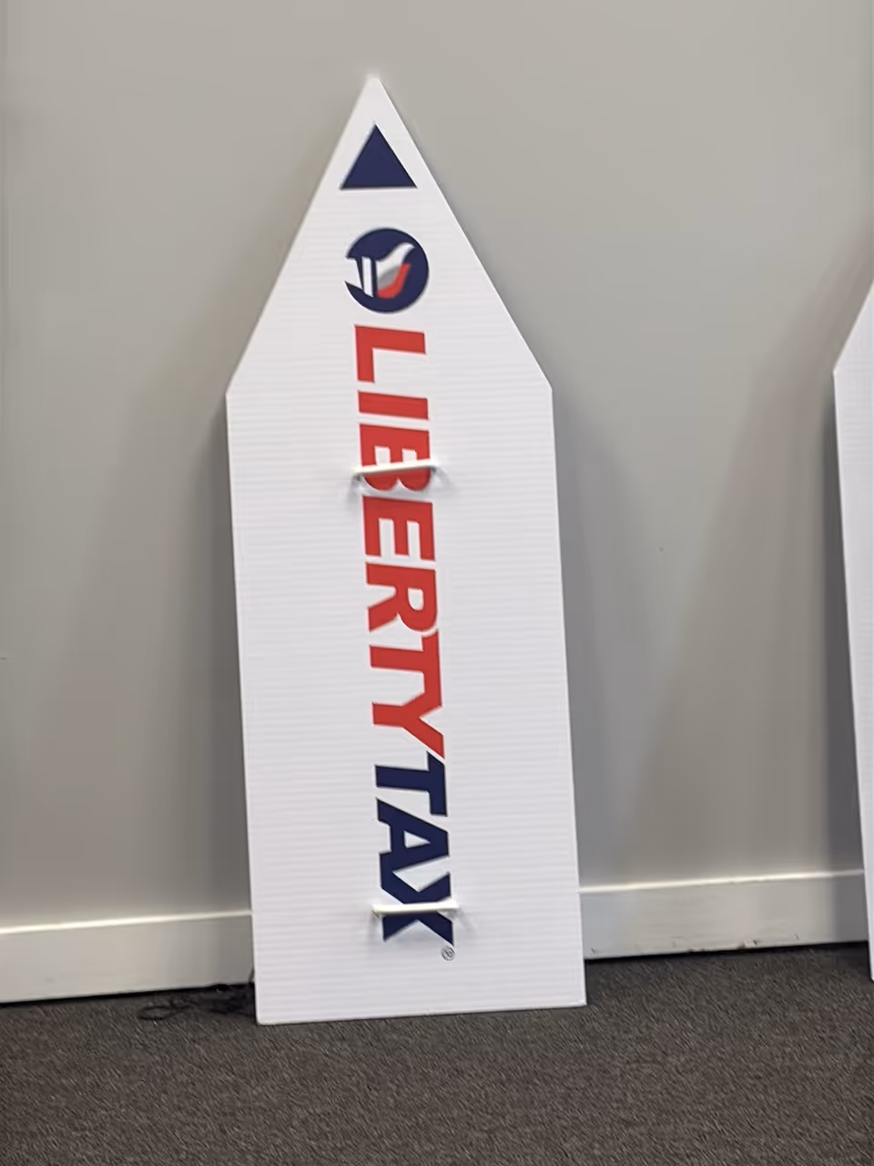 A white rocket-shaped sign with red LIBERTY TAX text leaning against a gray wall.
