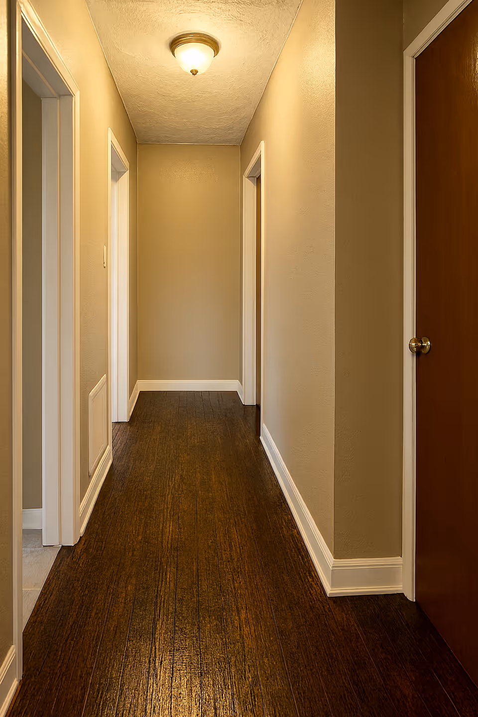 Narrow interior hallway in a senior living facility with doors along dark wood floor.