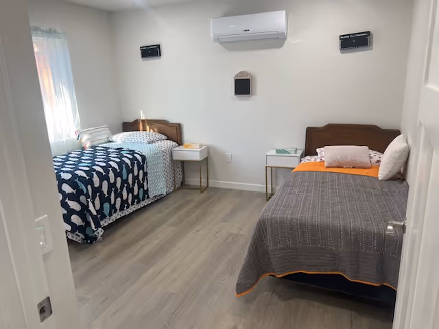 Shared senior living bedroom with two beds, nightstands, and a window.