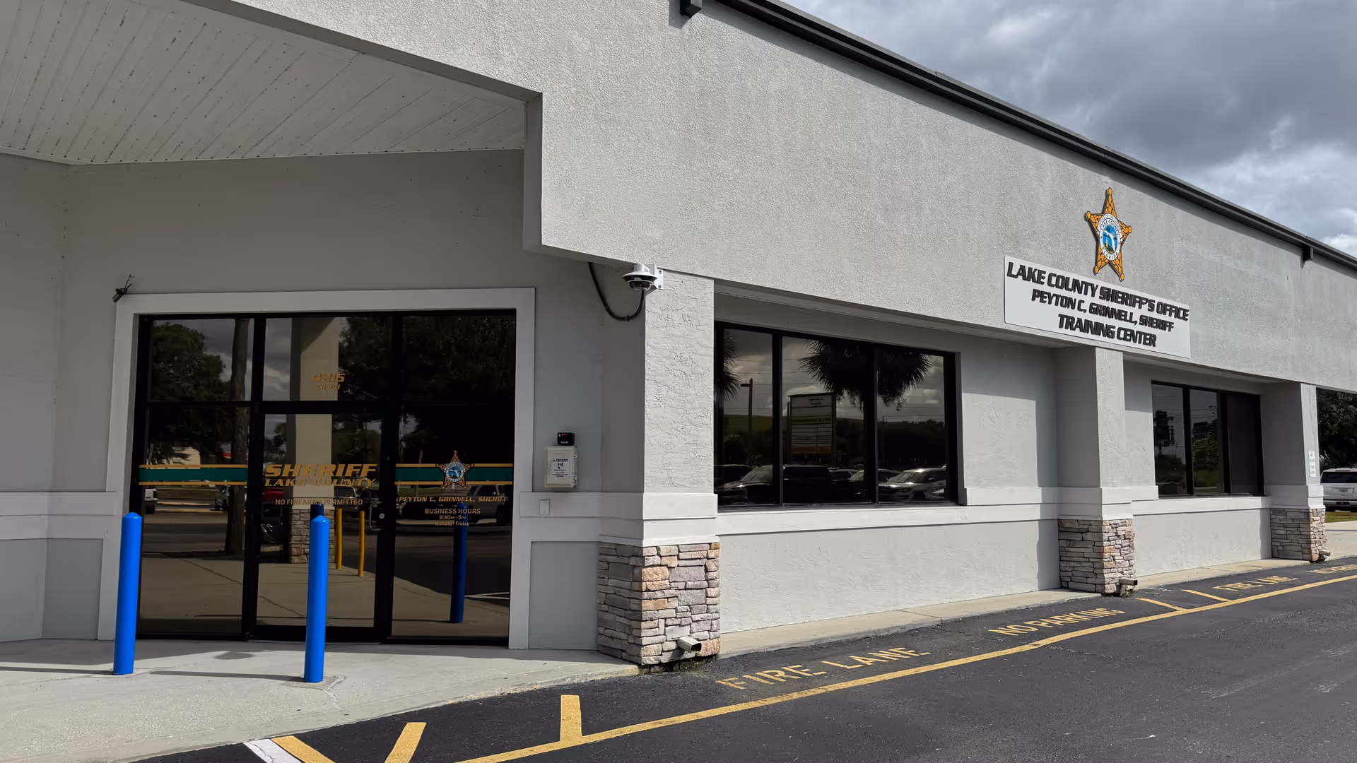 Exterior of sheriff's office building with glass doors and blue bollards.