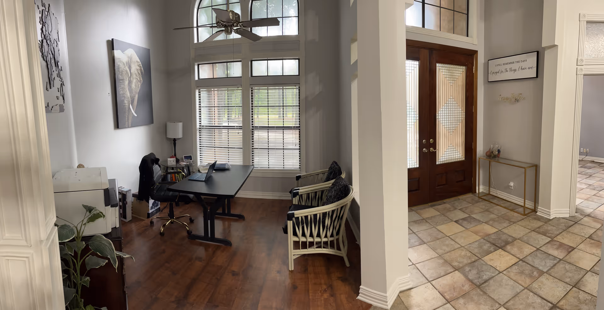 Office desk with computer and chairs in a bright lobby area near wooden double doors.
