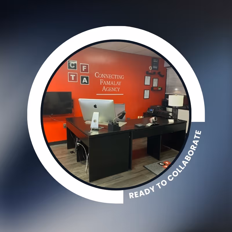 Reception area with red wall displaying Connecting Famalay Agency, desk, computer, and office supplies.