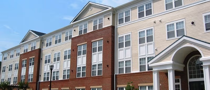 Front exterior of a multi-story brick-and-siding senior living building with many windows and an arched entrance.