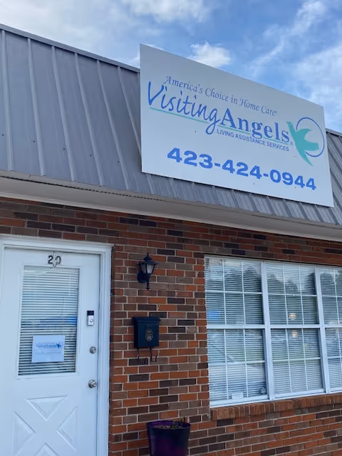 Brick building exterior featuring Visiting Angels sign, white door on left and large window on right.