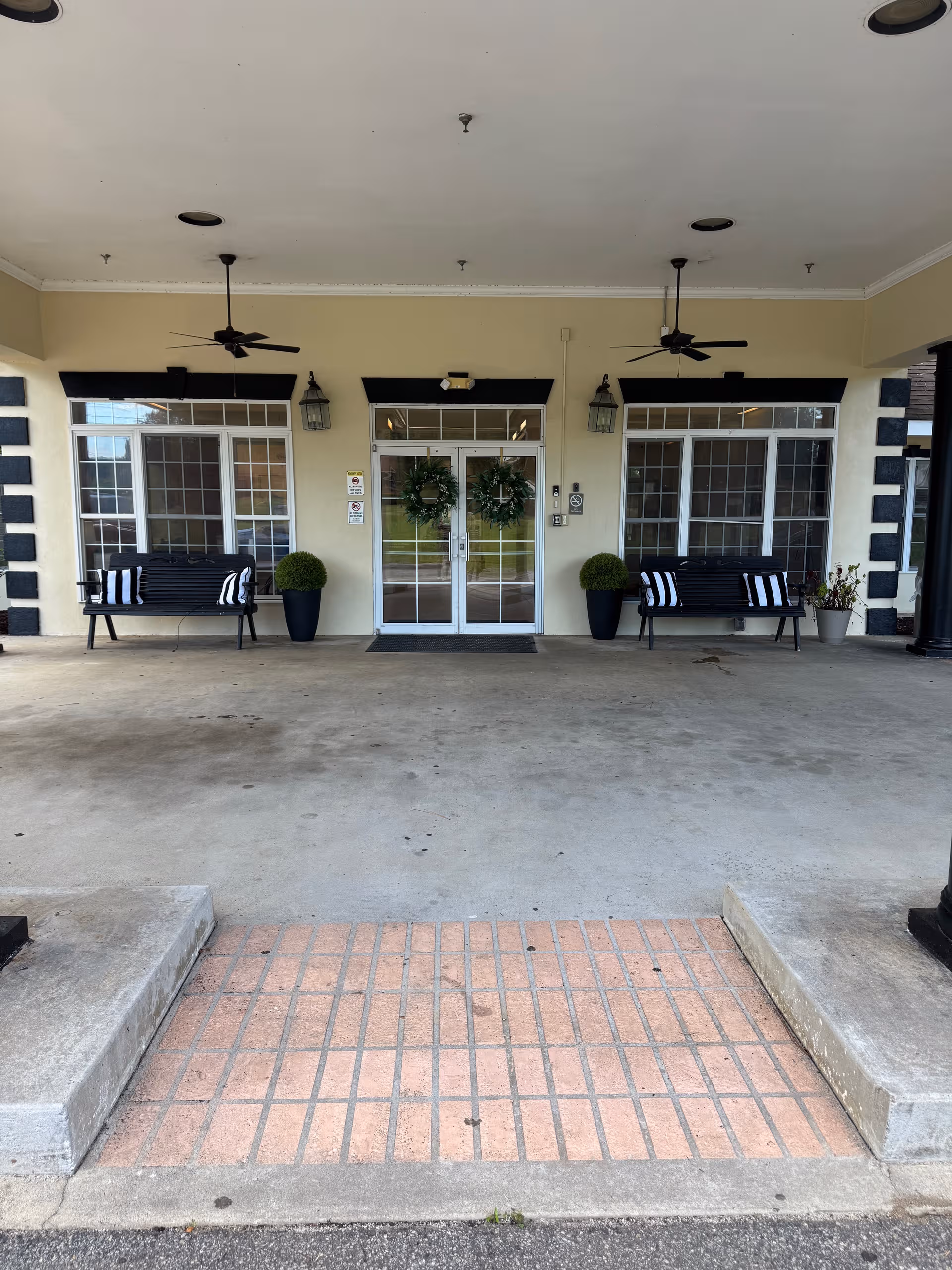 Senior living facility entrance on a covered porch with benches, wreaths, and potted plants.