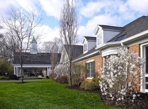 Exterior view of a brick senior living building with white flowering shrubs and manicured lawn.