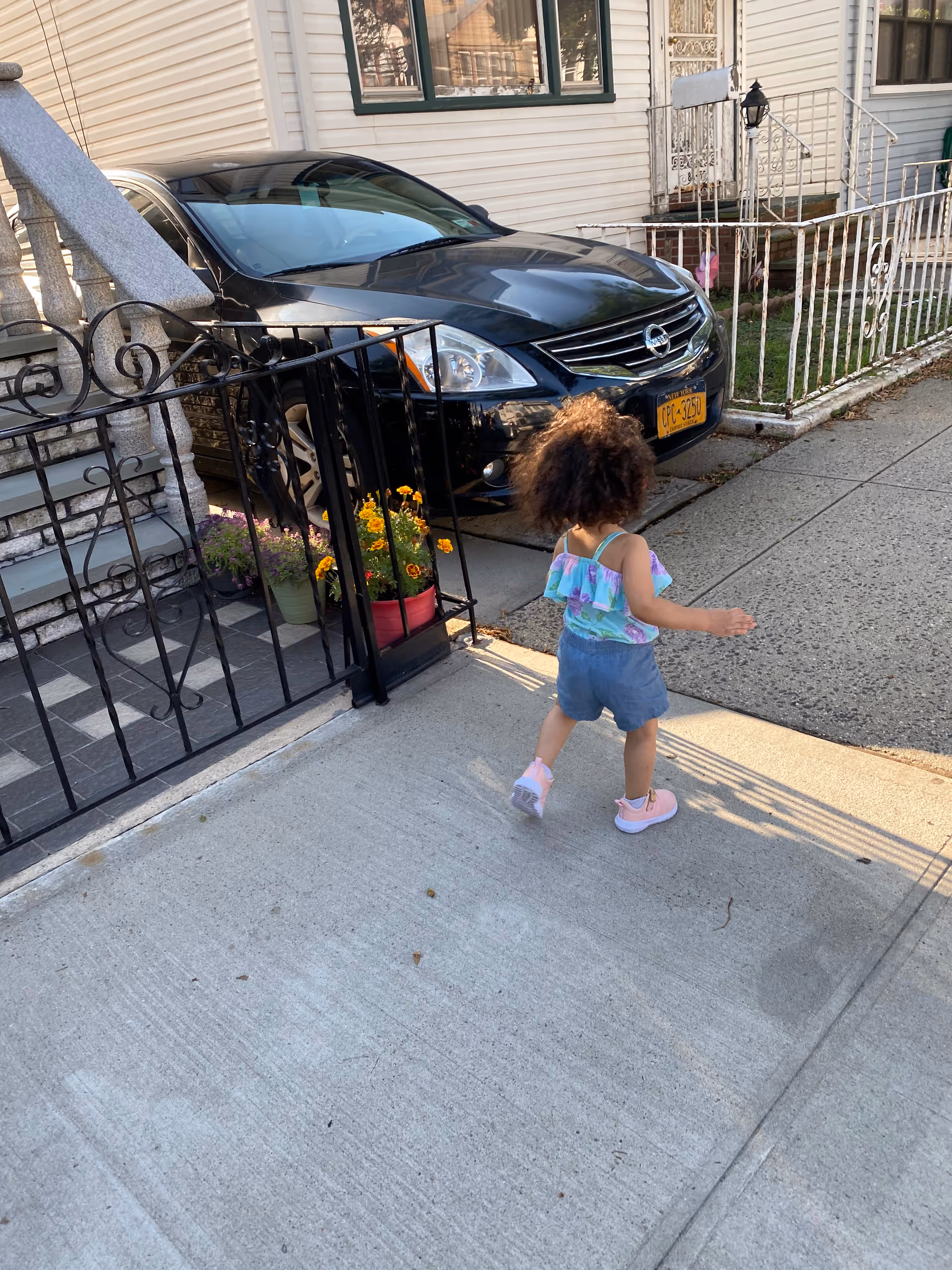 Child walks along sidewalk beside parked car in front of a residential building.