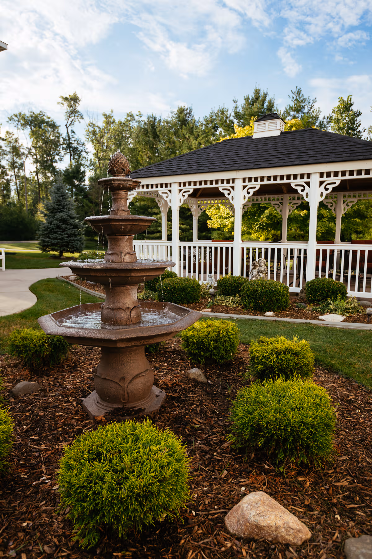 Stone tiered fountain sits in a landscaped courtyard with a white gazebo at Mercy Village
