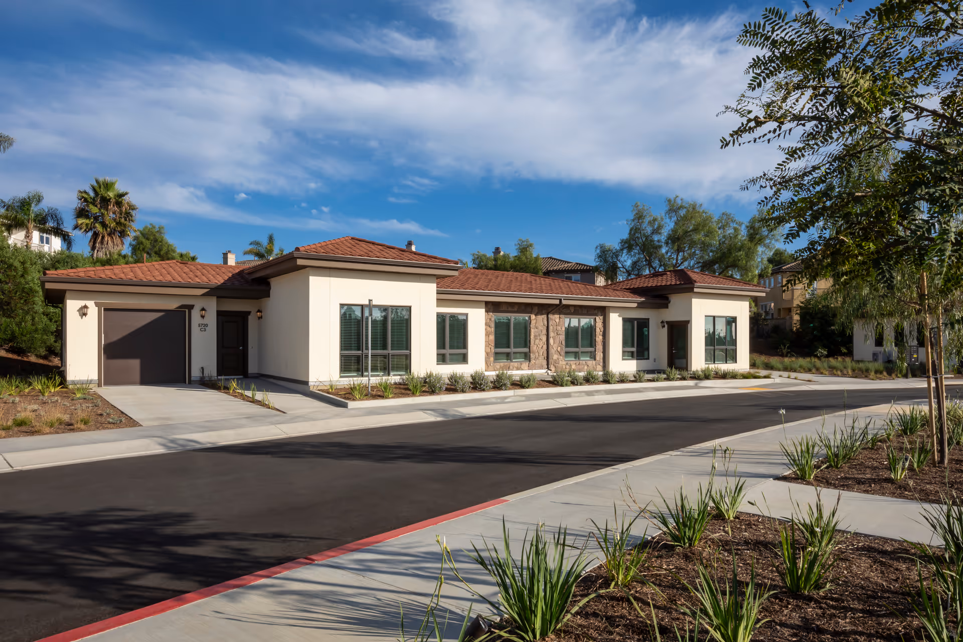 Single-story retirement facility front with red-tiled roof, paved road, and landscaped frontage.