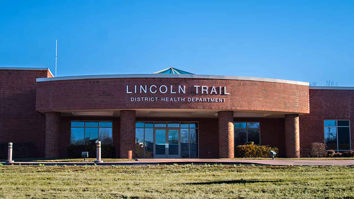 A brick Lincoln Trail District Health Department building with glass entry doors and a curved front.