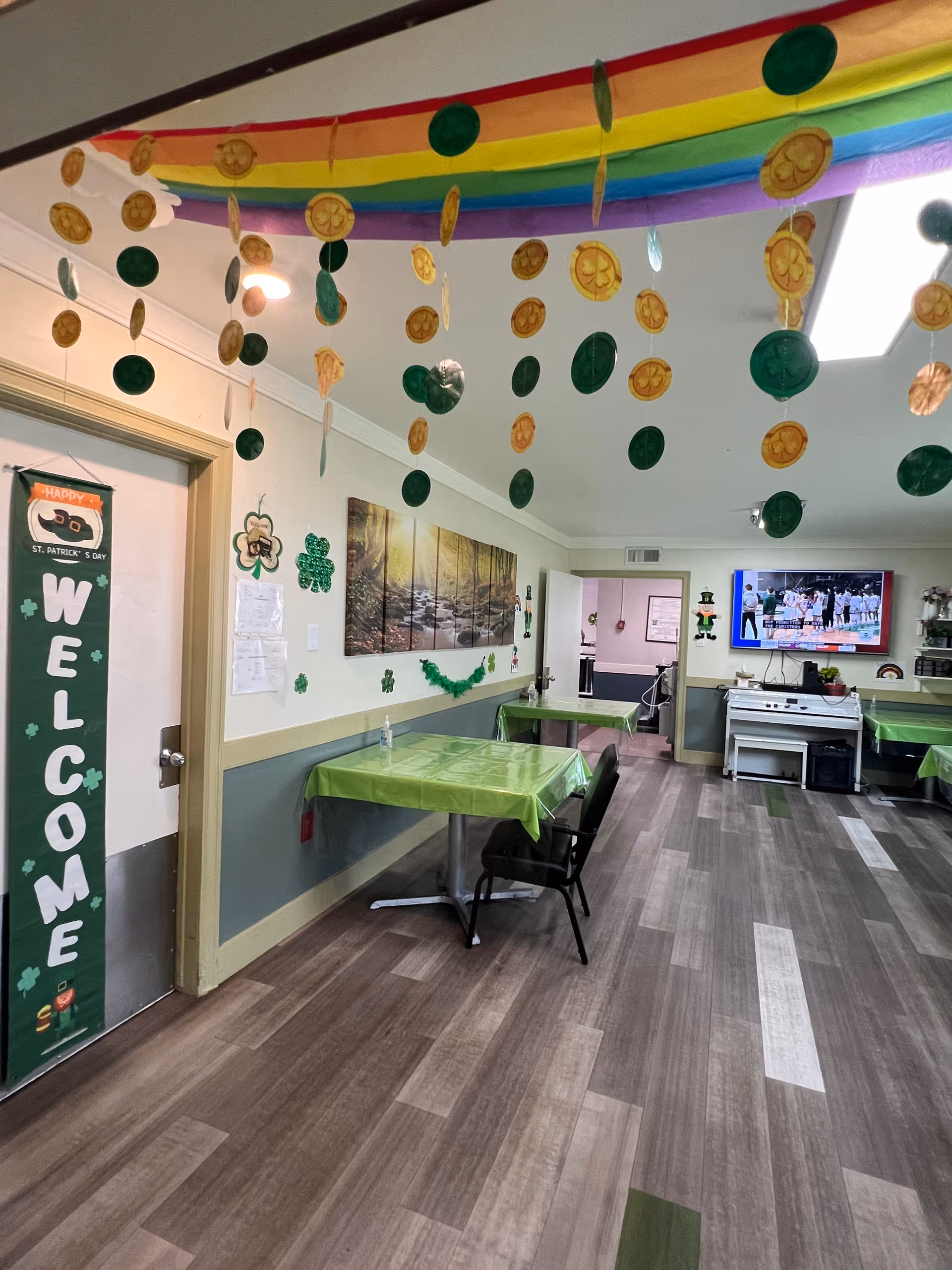 Interior senior living dining area with green tablecloths, festive decorations, and a TV.