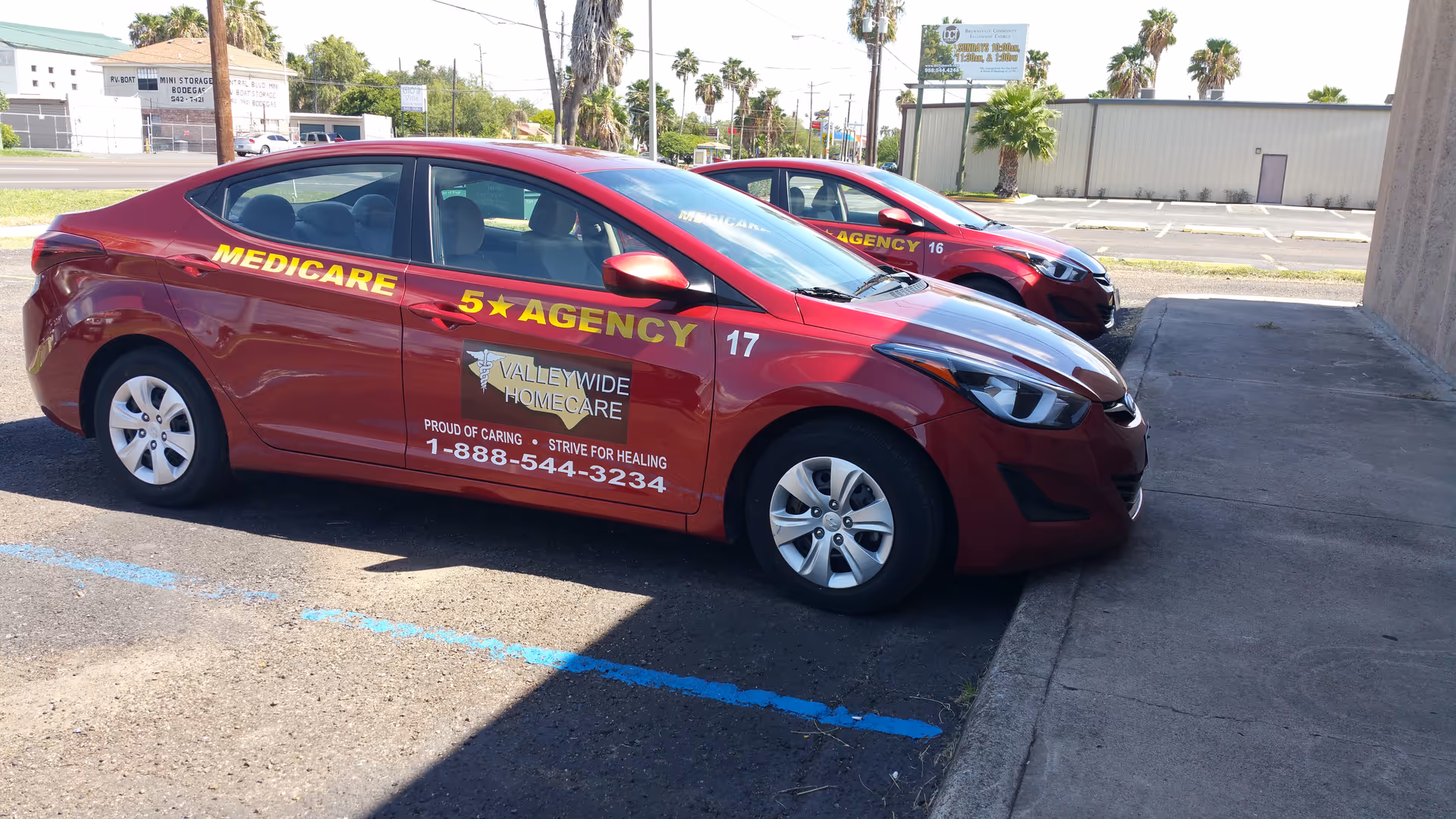 Two red Valleywide Home Care agency cars parked in a lot beside a building.