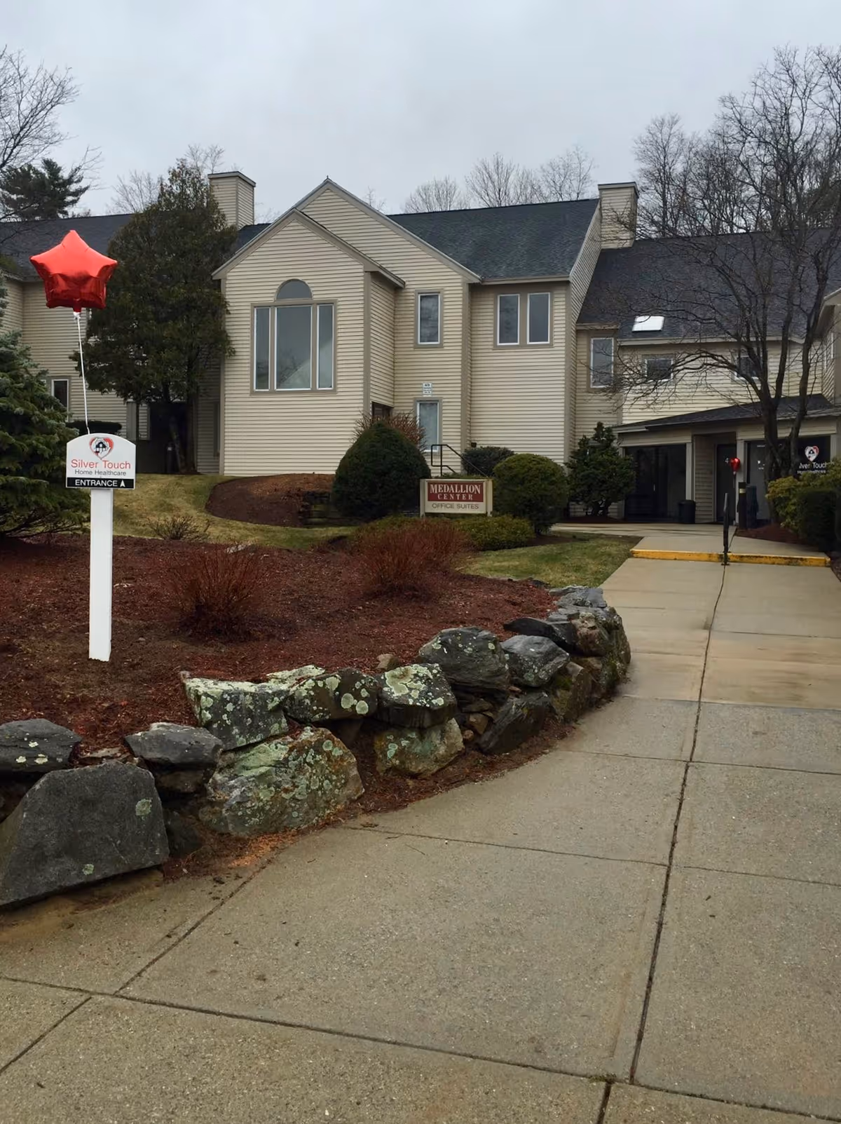 Exterior view of a senior living facility with a sign and landscaped entrance.