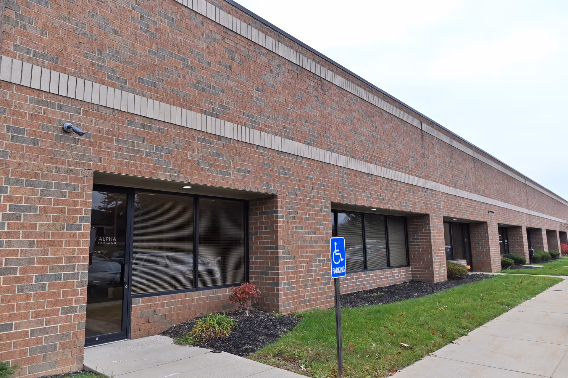 Brick exterior of Alpha Personal Care facility with windows and a handicap parking sign.
