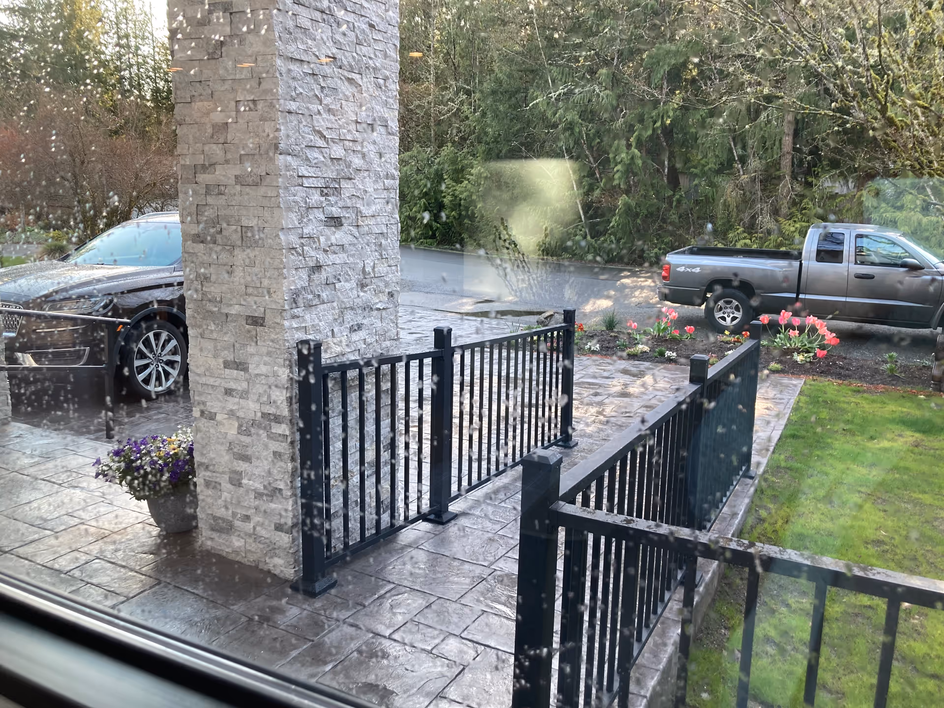 Exterior entrance of Sammamish Senior Living AFH with stone pillar, black railing, and parked cars.