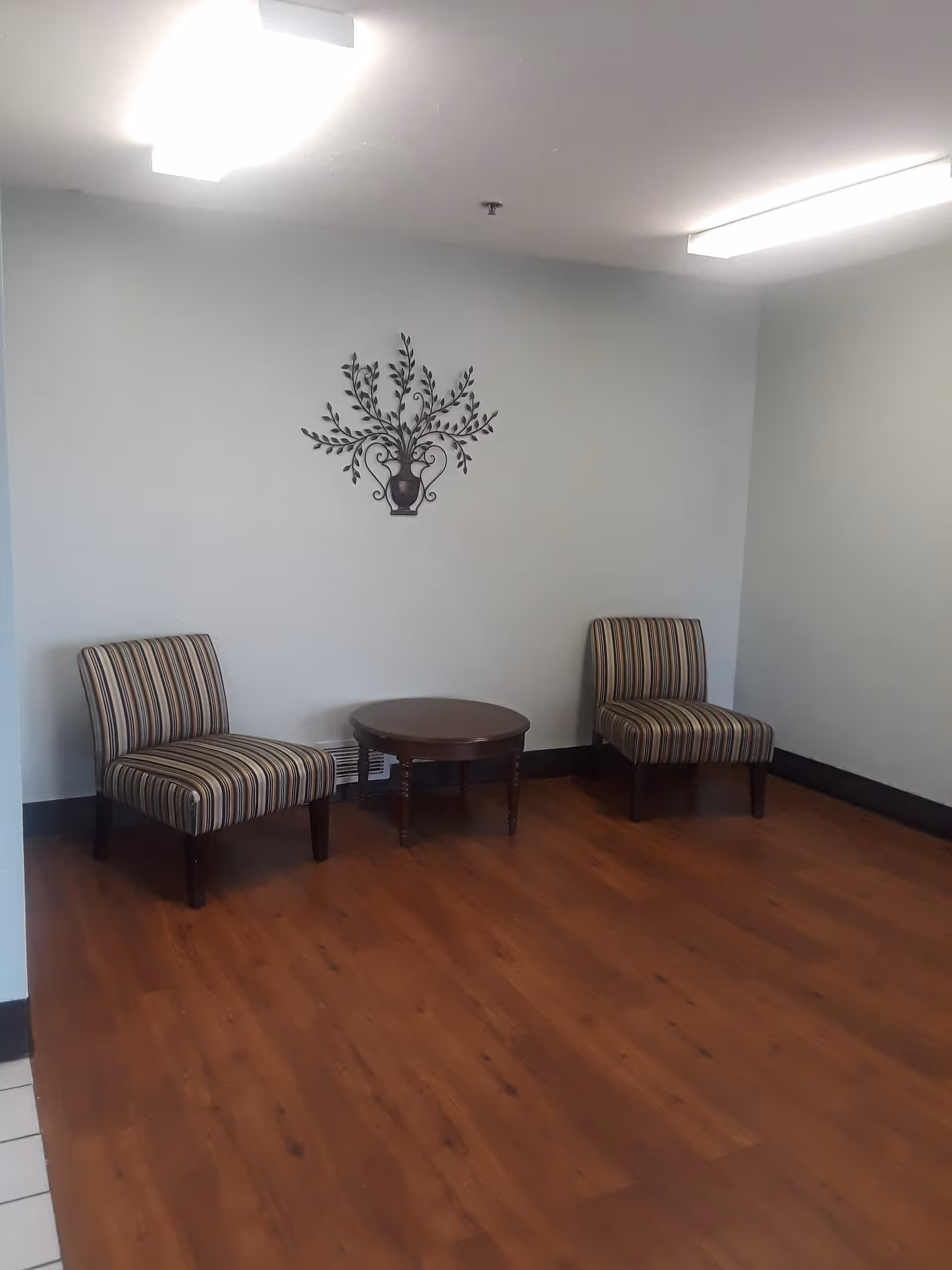 Small seating area with two striped chairs, a round table, and wall decoration.