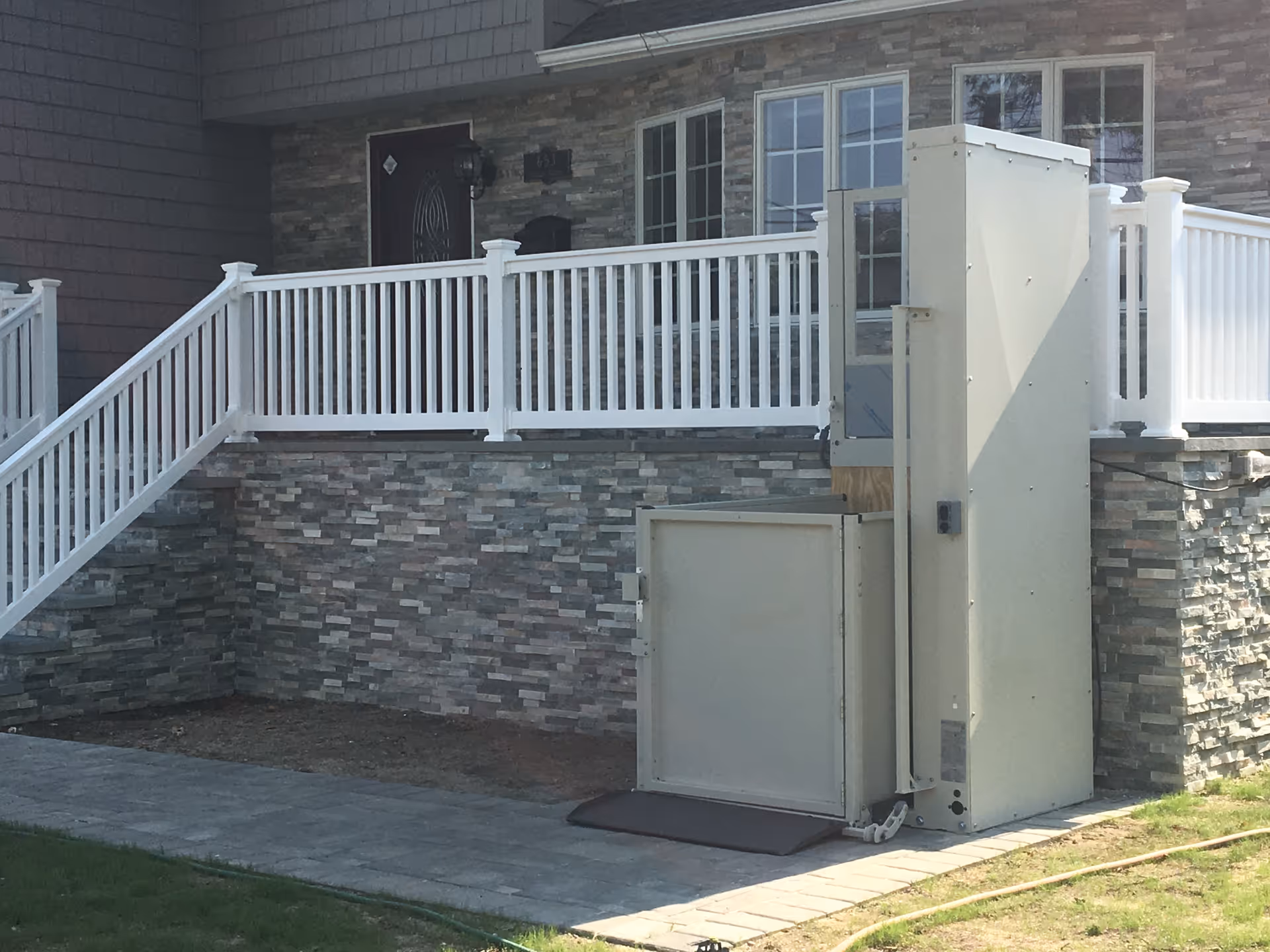 Residential exterior with white railing, stone facade, and a vertical outdoor lift beside stairs.