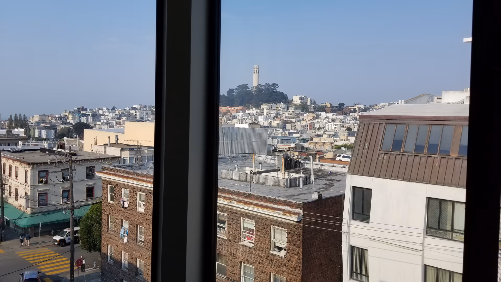 Urban city view through a tall window, rooftops in the foreground and a distant hill.