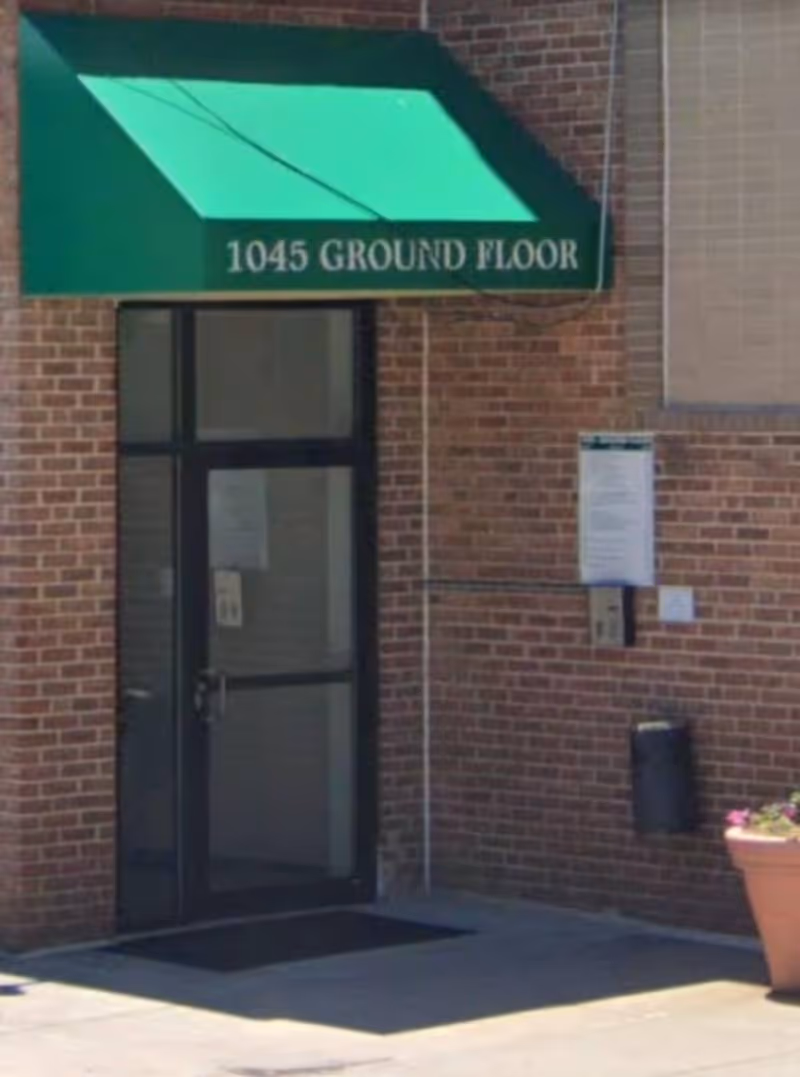 Brick building exterior with a glass door and green awning reading '1045 GROUND FLOOR'.