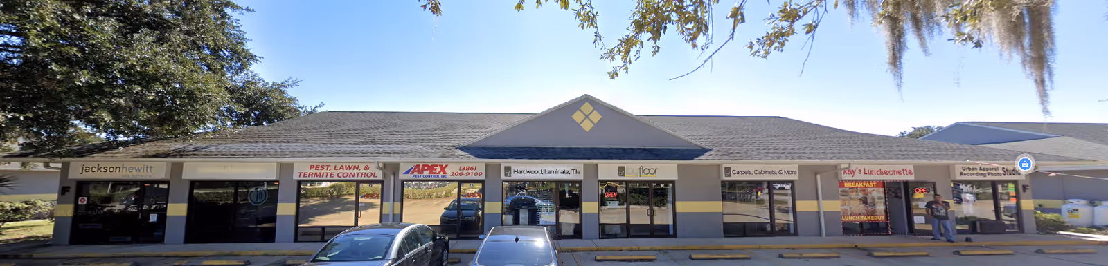 Front view of a single-story strip mall with multiple storefronts and parked cars.
