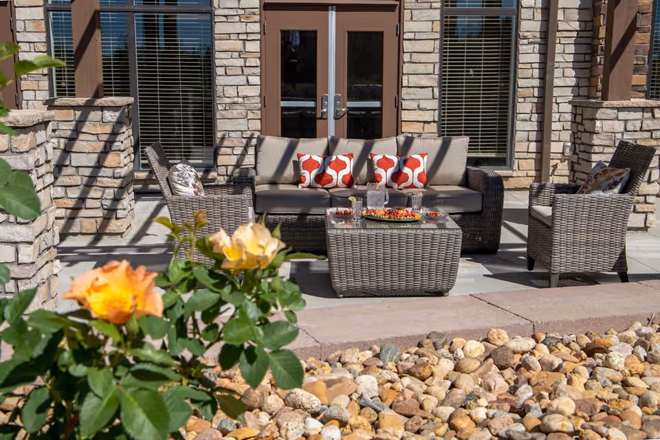 A cozy outdoor seating area with a couch and chairs surrounded by flowers and stones.