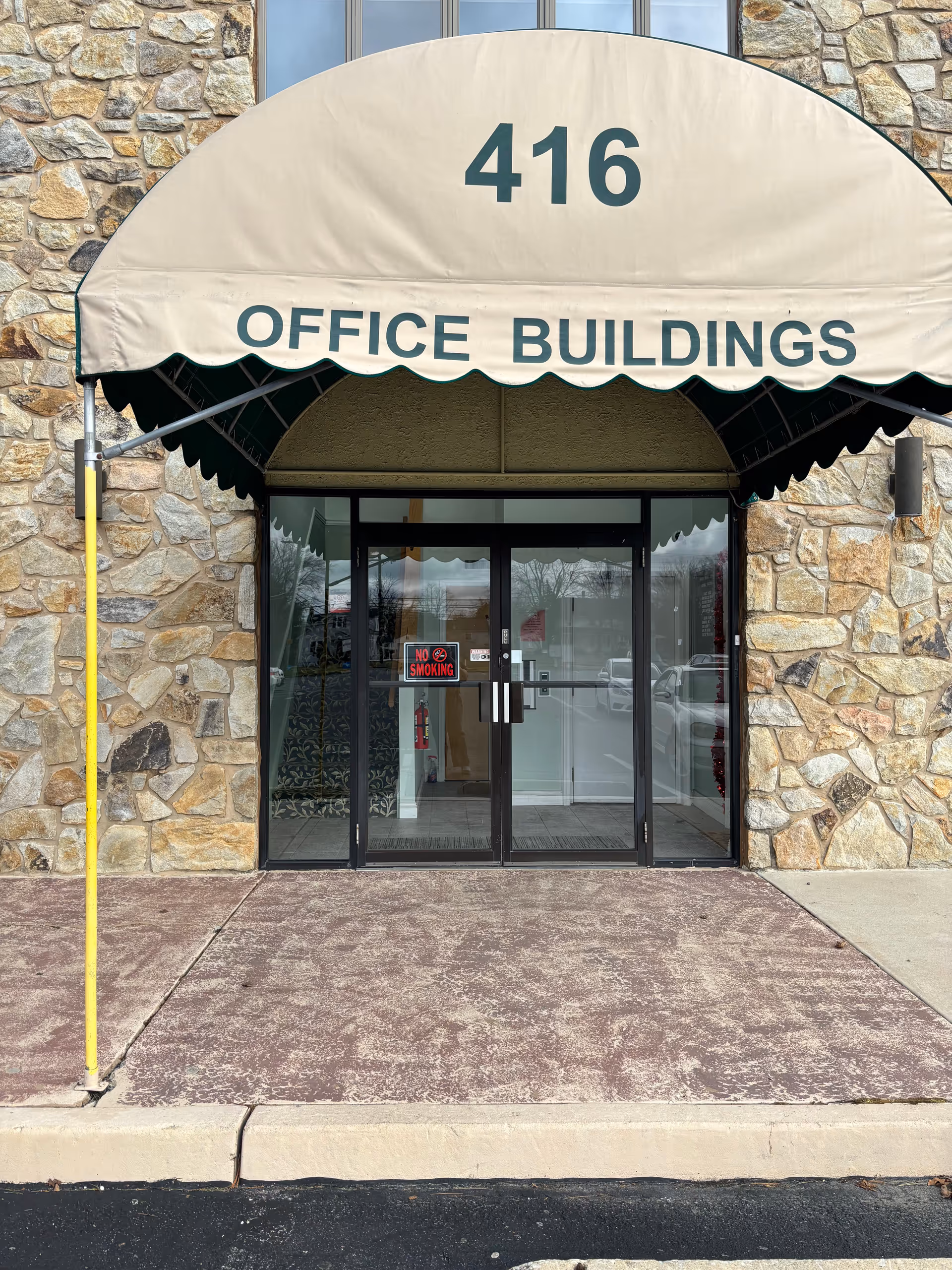 Stone facade entrance with beige canopy marked '416 Office Buildings' above glass doors.