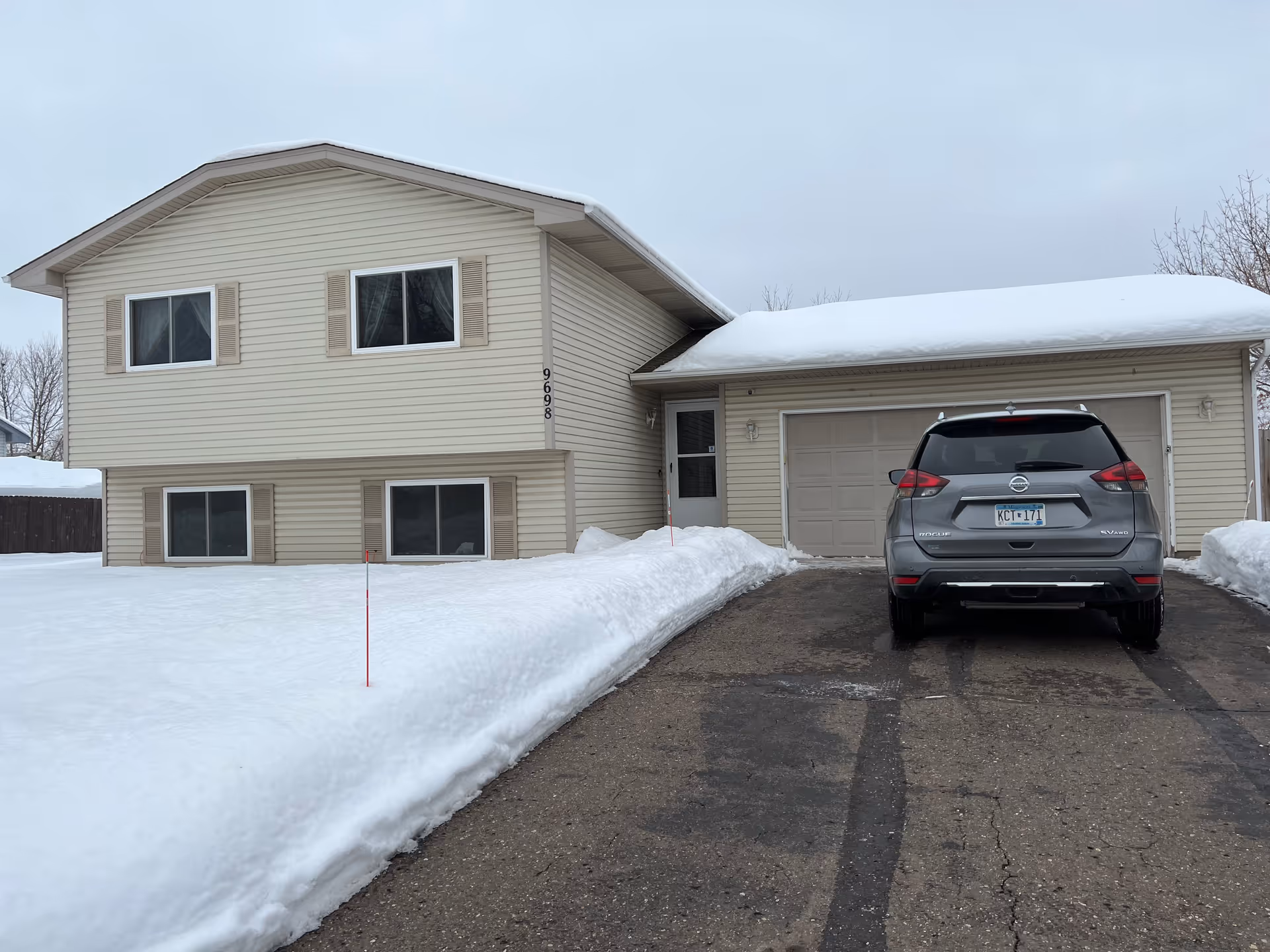 Suburban two-story beige house with attached garage and a parked SUV in snow.