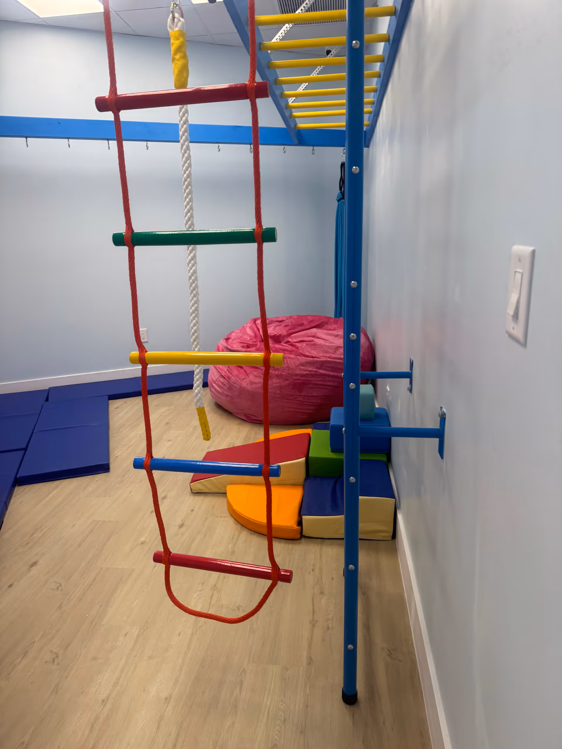 Indoor therapy playroom with climbing ropes, ladders, mats, and soft seating.