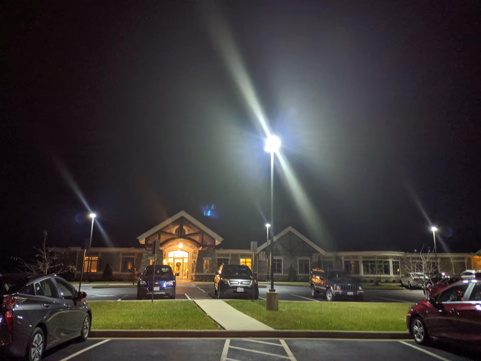 Night exterior of Lifecare Hospice building with illuminated entrance and several parked cars.