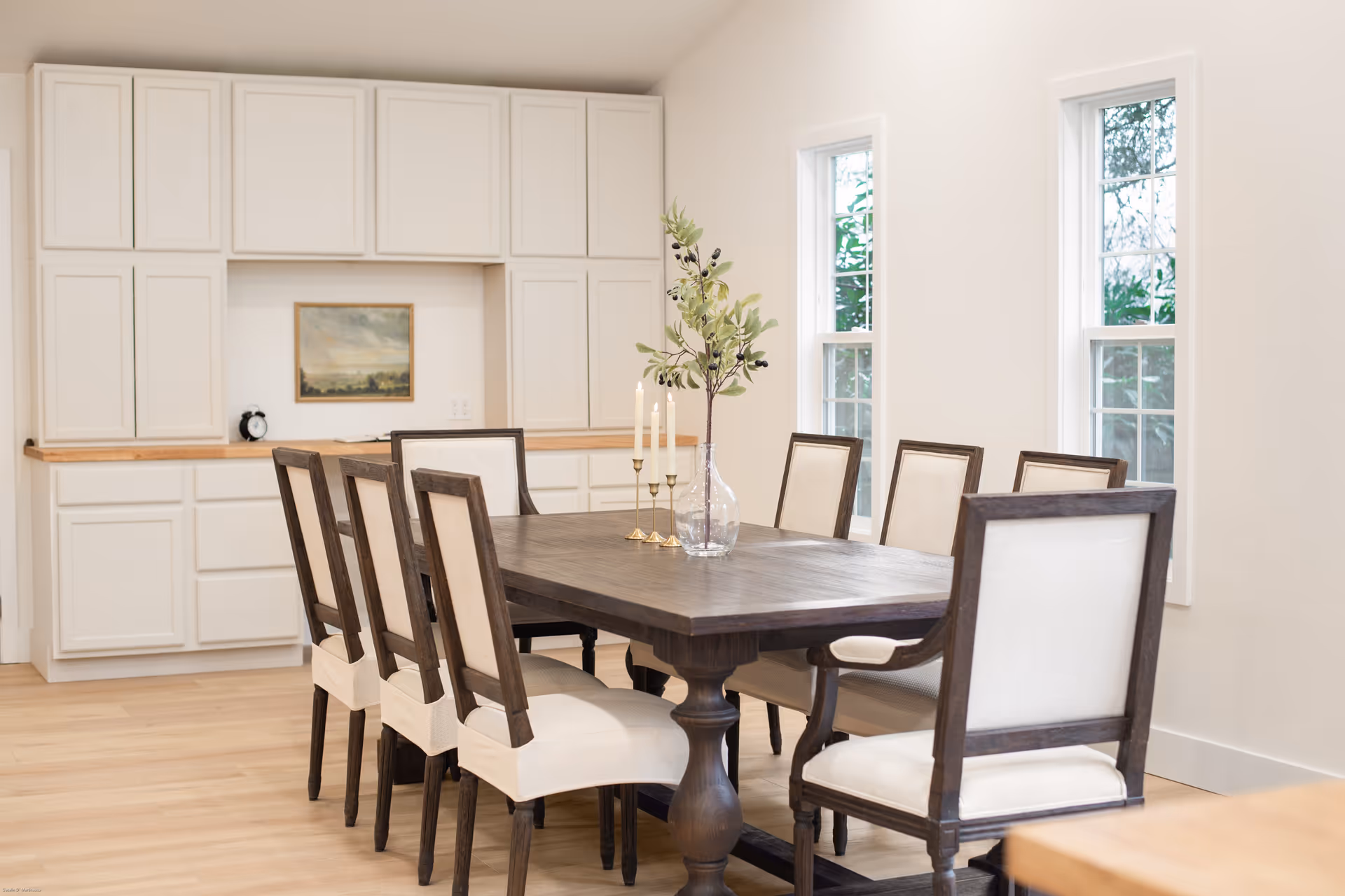 A large wooden dining table with eight upholstered chairs in a bright dining room.