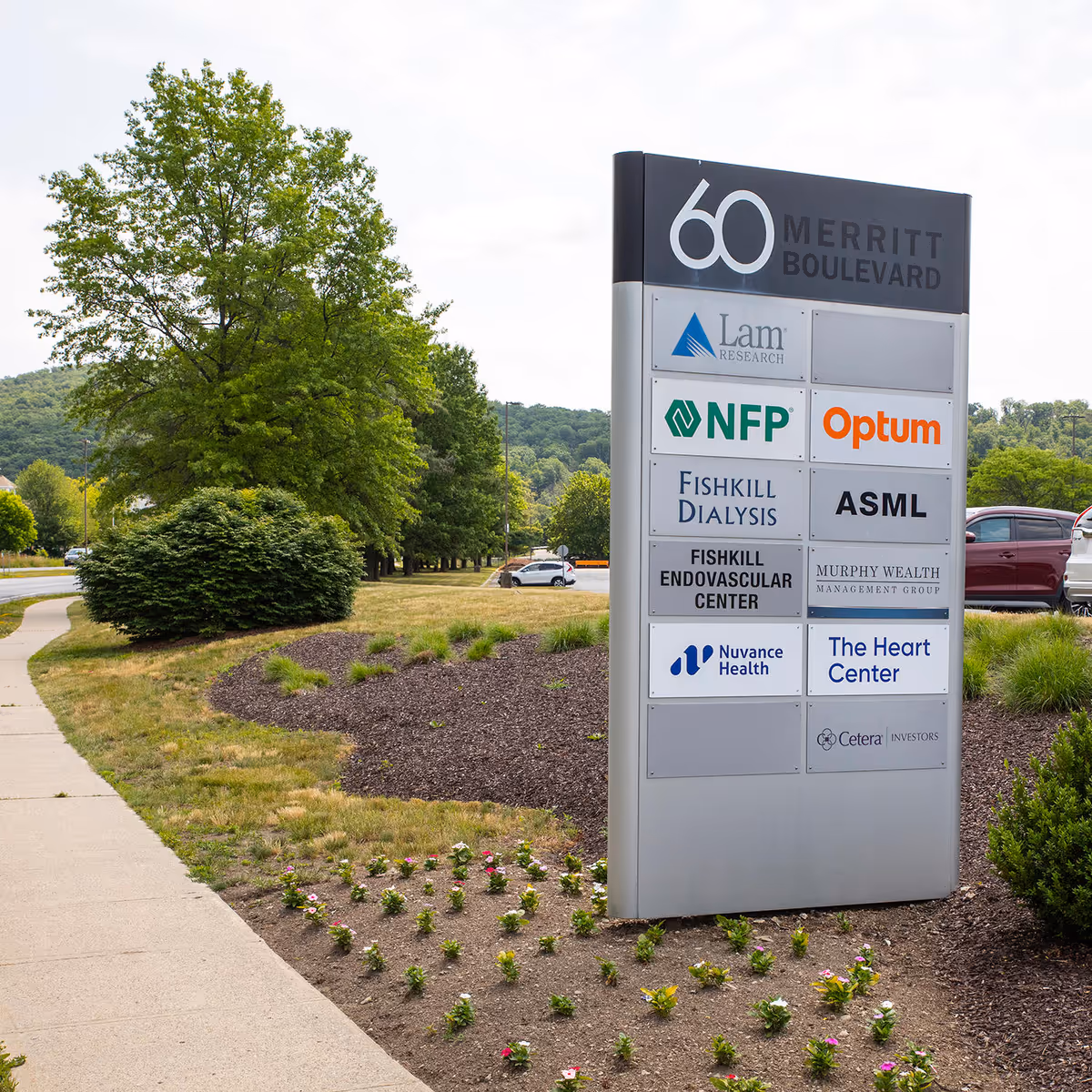 Exterior signboard displaying multiple medical center logos beside a sidewalk and landscaped area